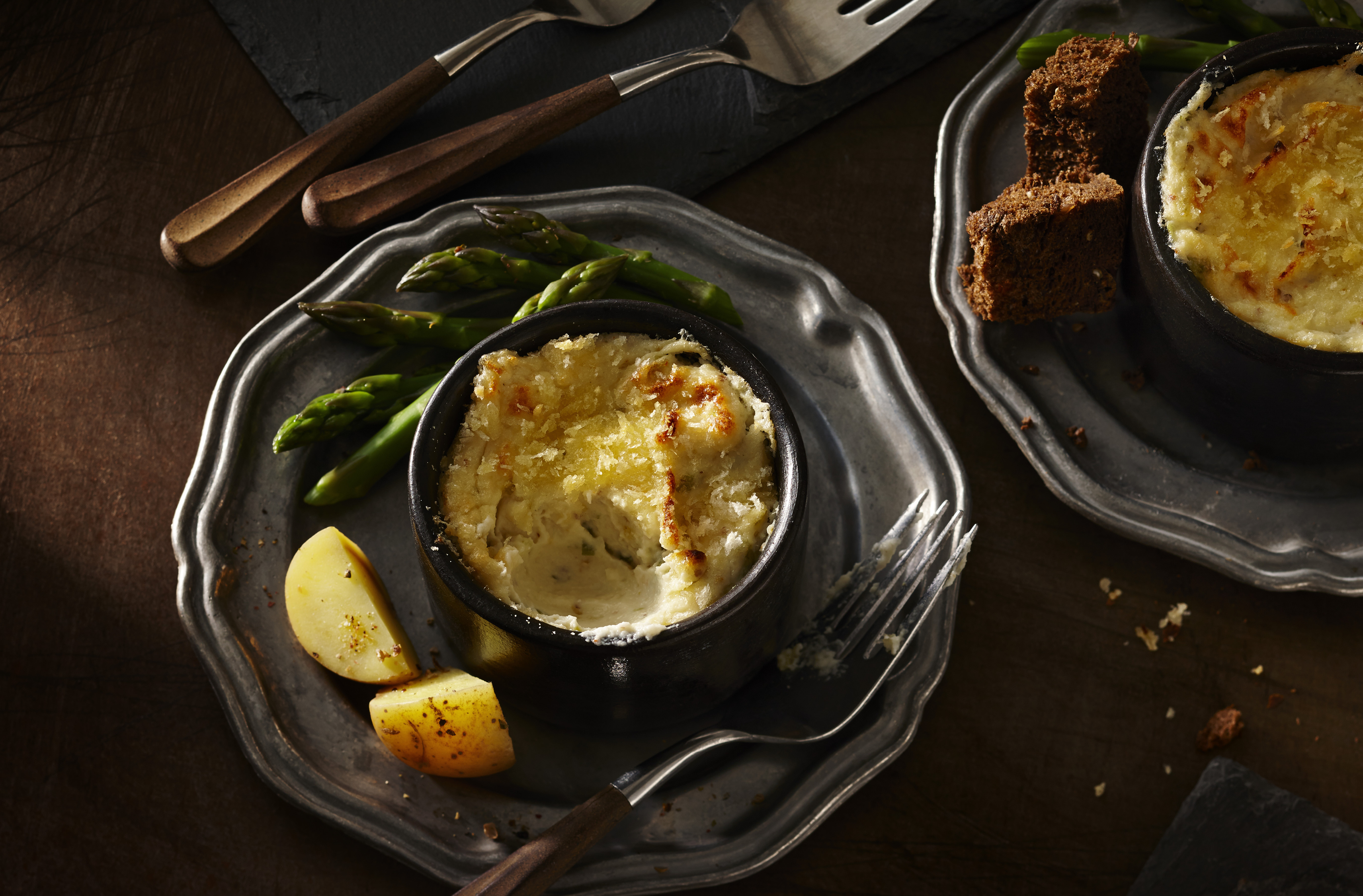 Bowl of cauliflower cheese fondue on a plate with asparagus & potato wedges
