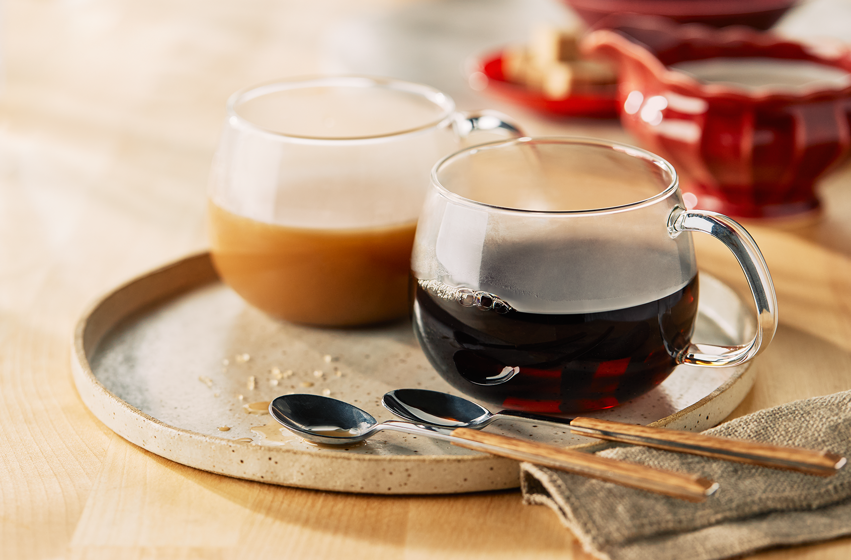 Two glasses of coffee, one with cream and one without, on a round serving tray with 2 spoons.