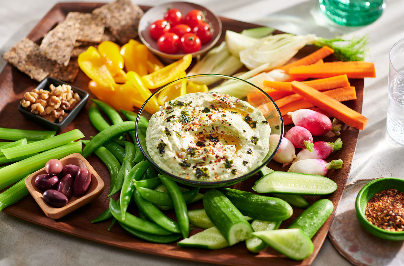 A sesame, nori and puréed edamame dip on a charcuterie style serving tray with an array of fruits, veggies, olives and breads for dipping.