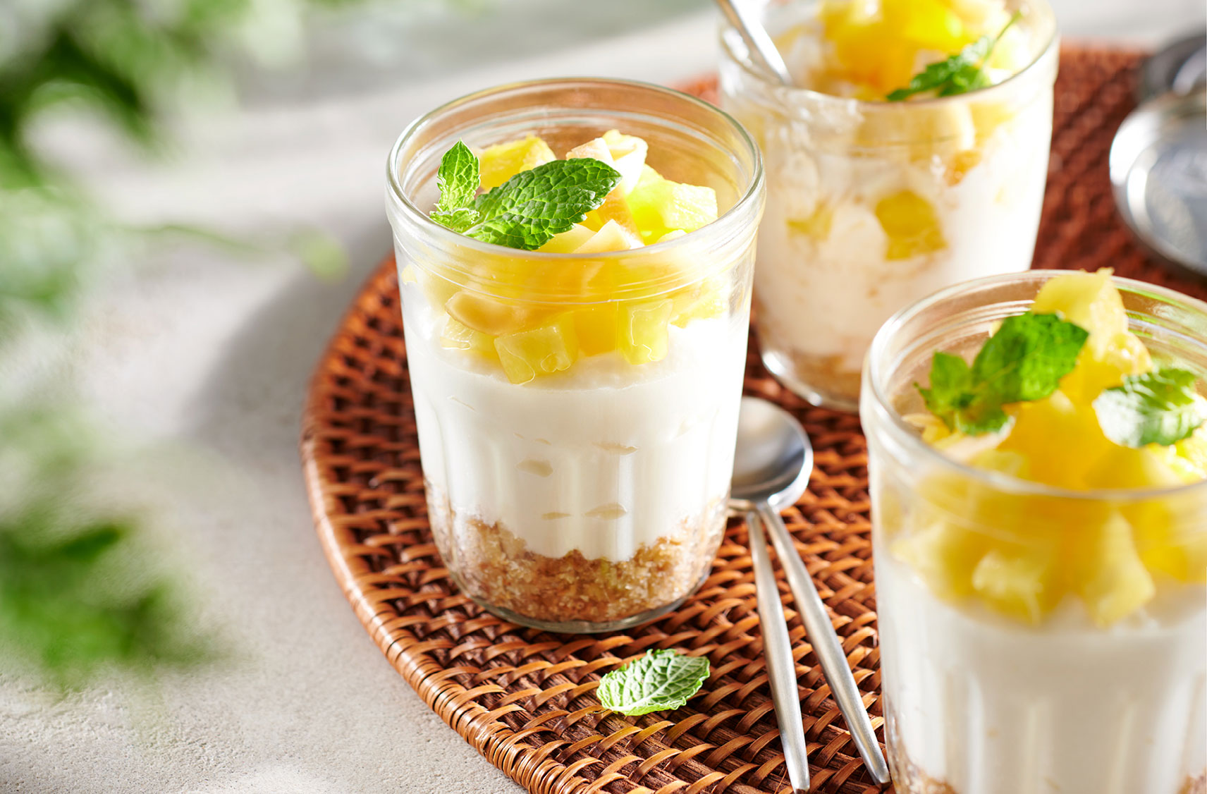 Three glasses filled with a no bake style of coconut and pineapple plant-based cheesecake on a wicker serving plate.