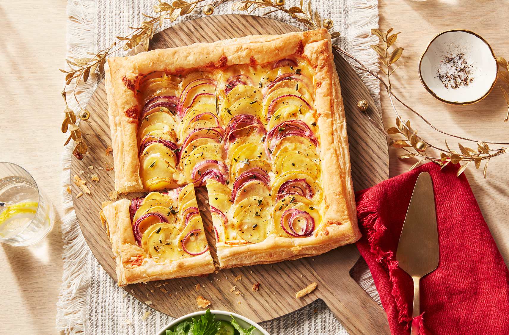 Une tarte rustique aux pommes de terre, au cheddar et à la crème sure fraîchement sortie du four, dont un coin est coupé et prêt à être servi, sur une planche à découper.