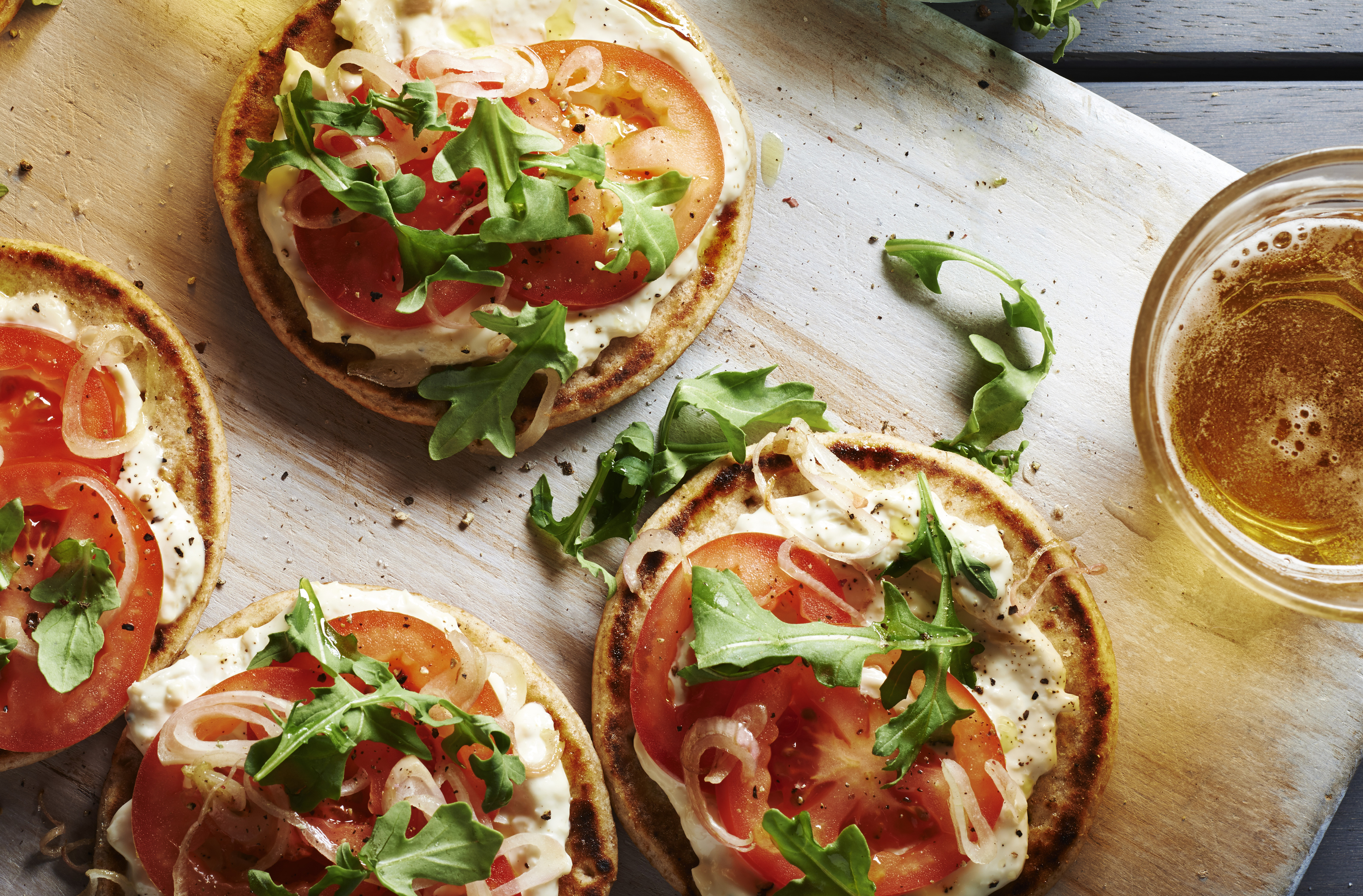 Cinq mini pizzas sur pain naan garnies de trempette aux artichauts et à l'asiago, de tomates et de roquette
