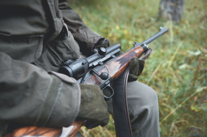 Carrying the rifle scope during hunt. Man sitting waiting in forrest. 