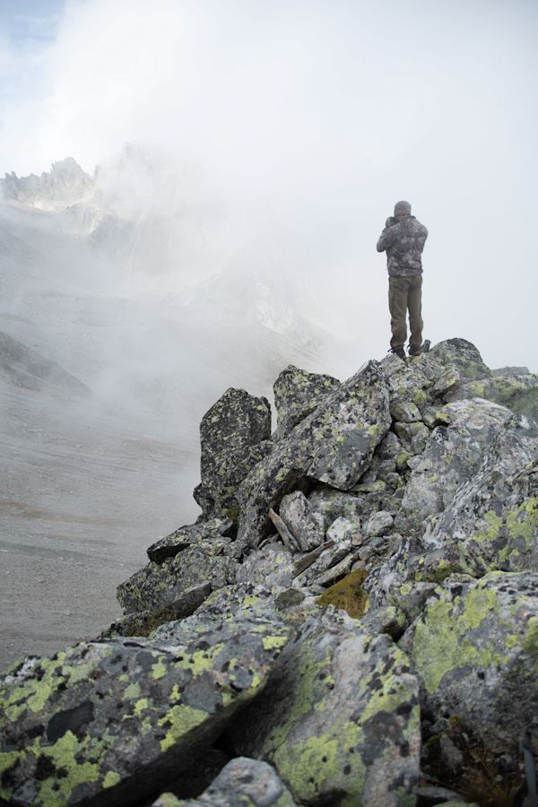 Hunting chamois with the EL Range TA in the Swiss Alps, hunter standing on rocks with binoculars