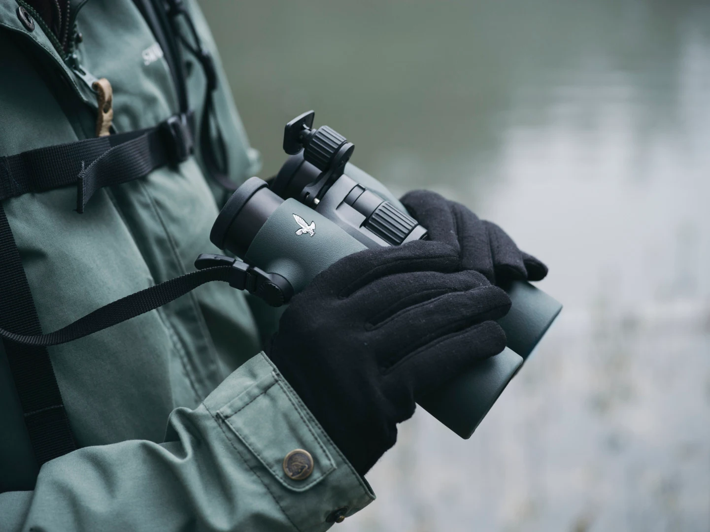 Observer holding a green Swarovski NL Pure binocular beside a backpack