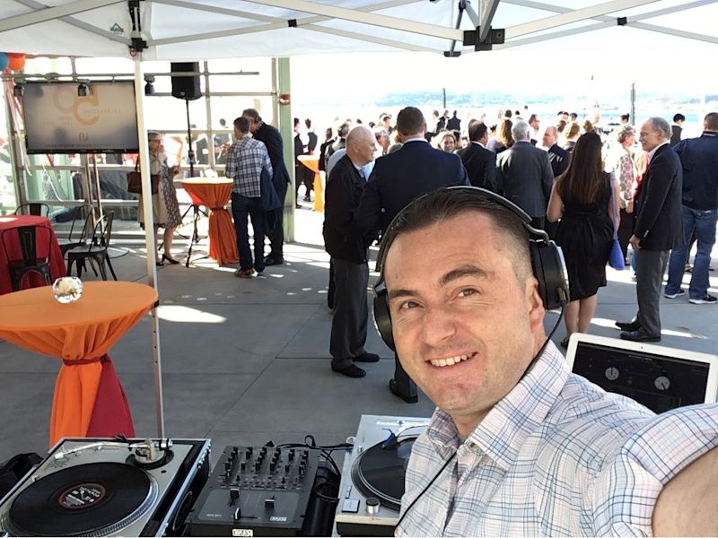 DJ Audeos with headphones at the turntable setup during a corporate event on the waterfront deck behind Pike Place Market in Seattle
