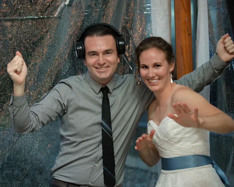 DJ Audeos with headphones and bride smiling together at the DJ booth during a wedding reception in Shelburne, Vermont