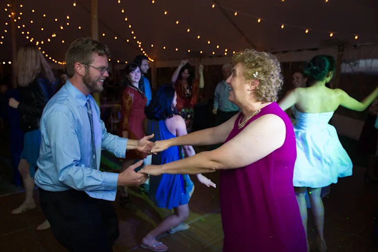 Wedding guests dancing and laughing on a packed dance floor under string lights at a reception in Shelburne, Vermont