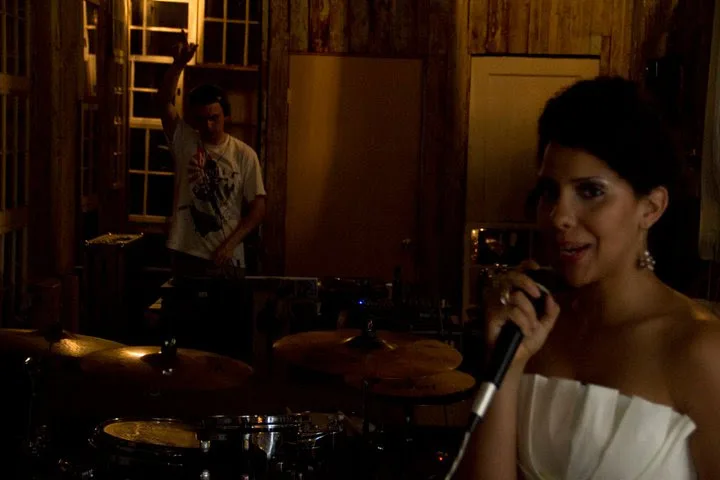 A singer in a white dress on the mic in the foreground while DJ Audeos works the decks in the background at the Philadelphia Printworks Launch Party