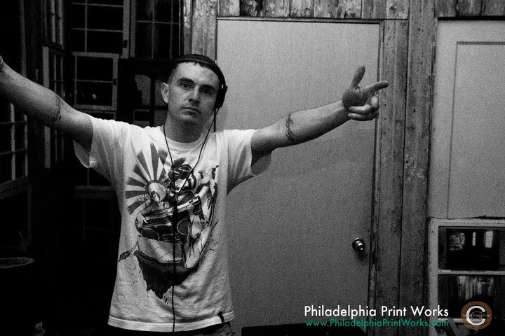 DJ Audeos in headphones at the Philadelphia Printworks Launch Party, throwing arms wide in a black-and-white shot watermarked with the PPW logo