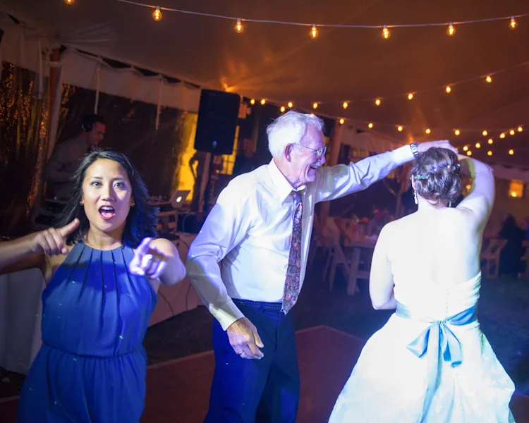 Bride being spun on the dance floor by guests under string lights at a Shelburne, Vermont wedding reception