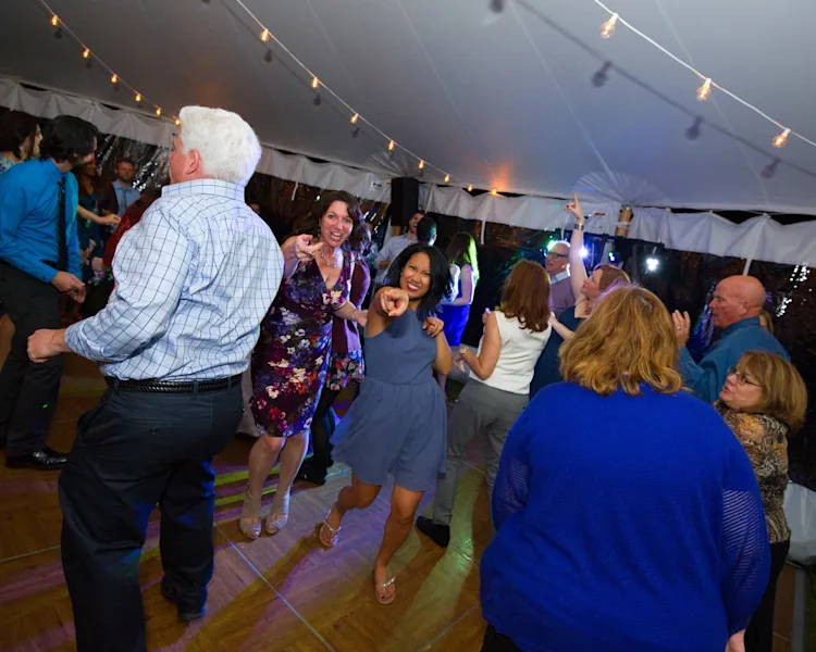 Guests laughing and dancing together on a packed dance floor under string lights at a wedding reception in Shelburne, Vermont