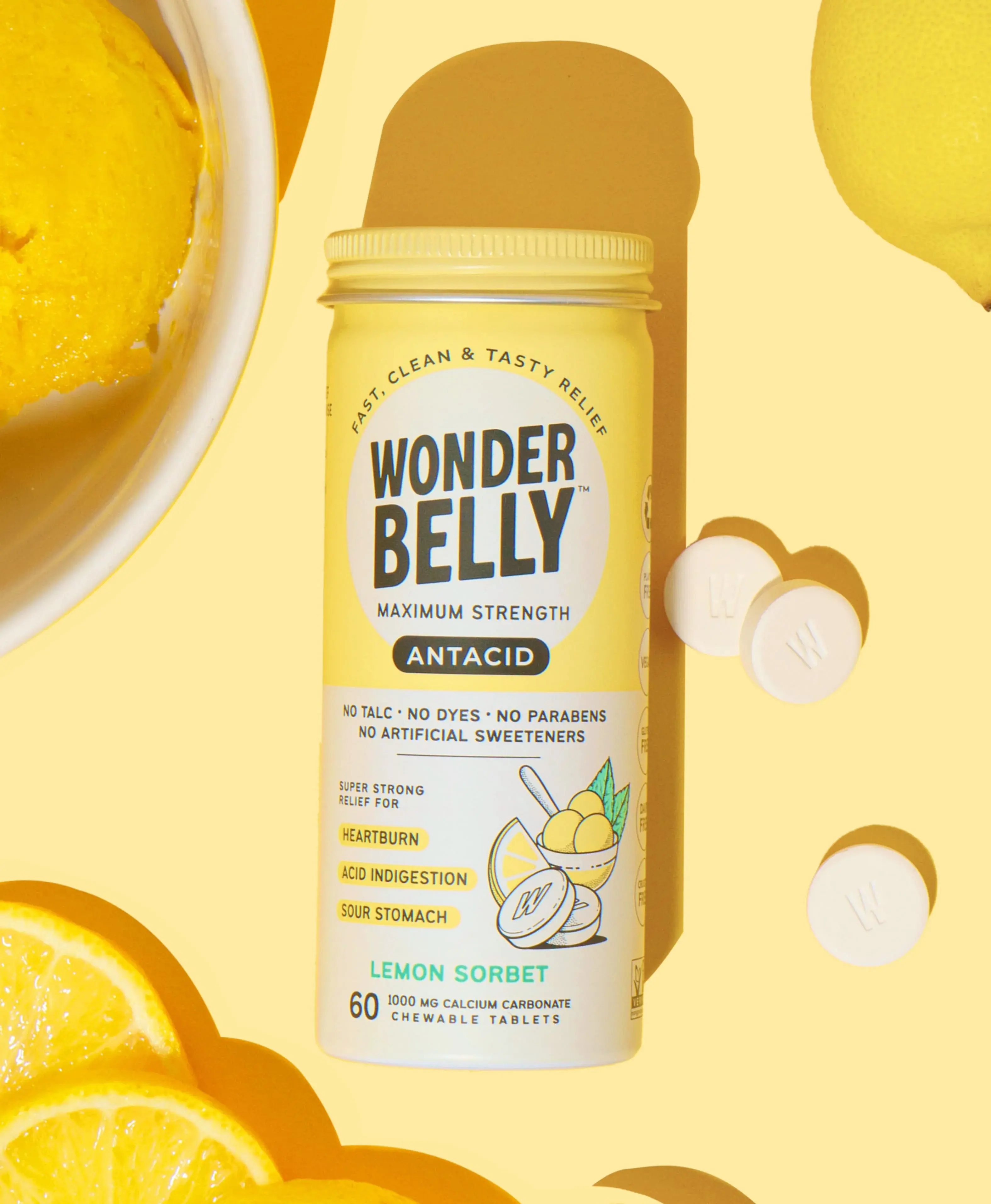 Wonderbelly maximum strength antacid bottle labeled “Lemon Sorbet,” shown with white chewable tablets, lemon slices, and a bowl of yellow sorbet on a bright yellow background.