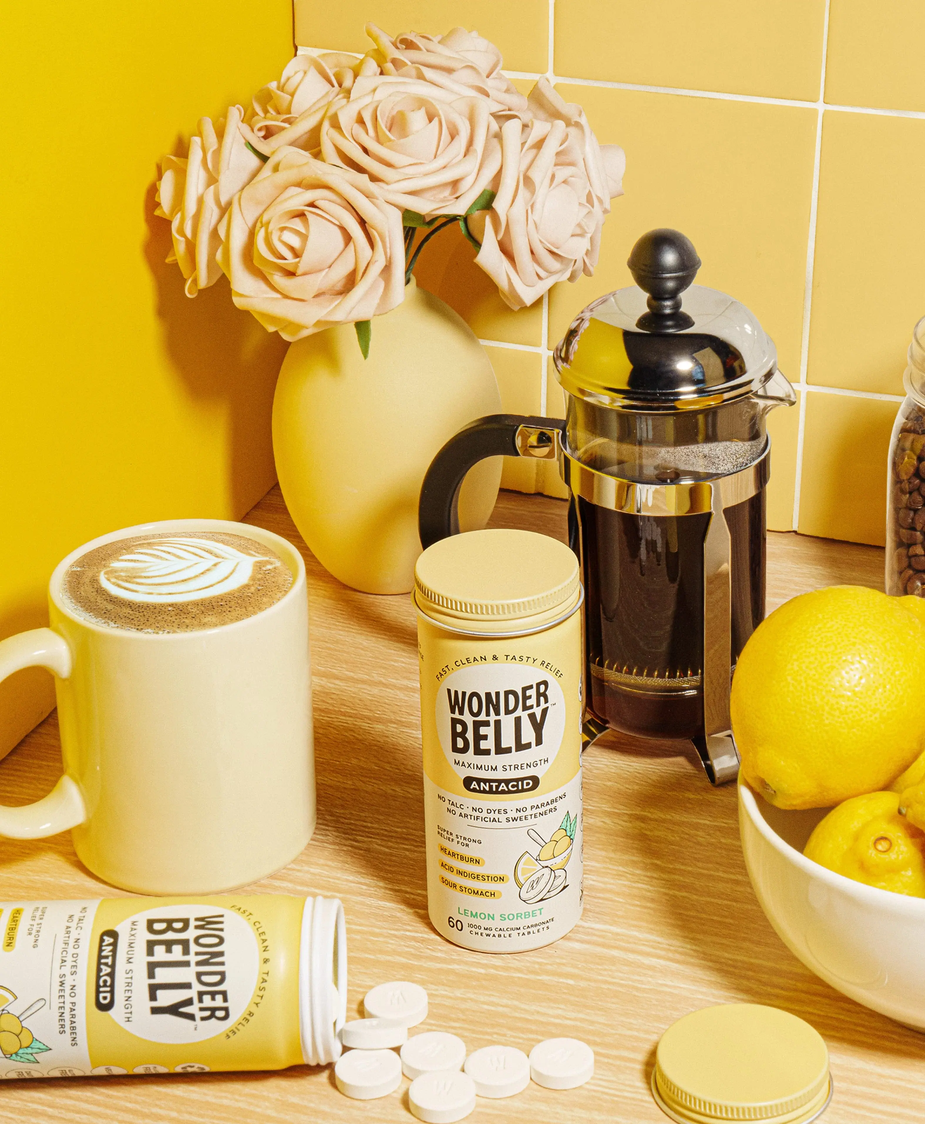 Wonderbelly maximum strength antacid bottle labeled “Lemon Sorbet,” shown with white chewable tablets, lemon slices, and a bowl of yellow sorbet on a bright yellow background.