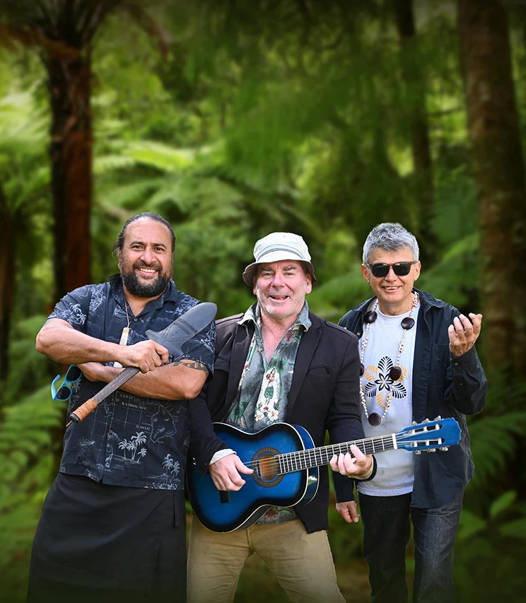 Three men standing in native bush - one with a short club, one with a blue guitar and one wearing a Pacific shell neck ornament.