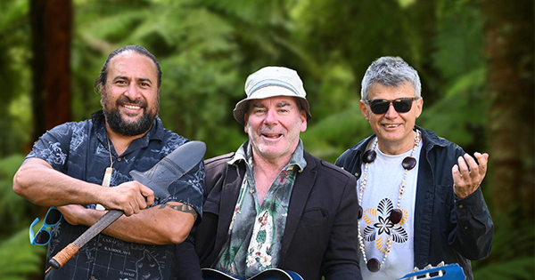 Three men in native bush - one with a taiaha, one with a blue guitar and one wearing a Pacific shell neck ornament.