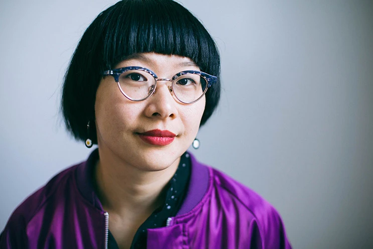 Close up photo of a Chinese woman wearing tortoiseshell glasses and a purple jacket.