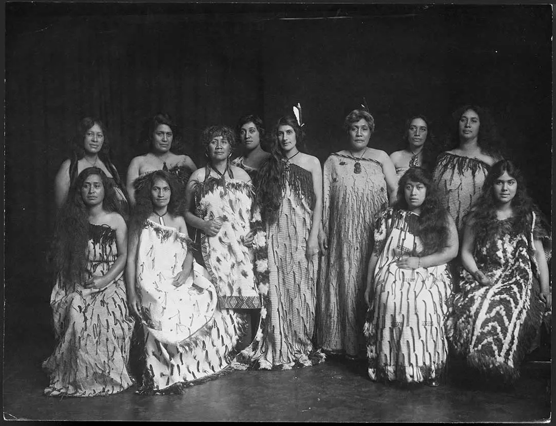 A group of wāhine Māori wearing kākahu (cloaks) and korowai (cloaks decorated with tags). 2 wāhine Māori in the centre are wearing feathers in their hair.