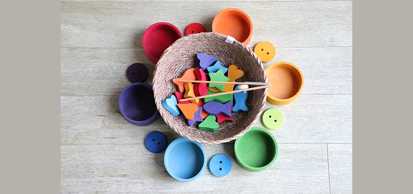 Brightly coloured bowls and buttons around a basket containing different coloured shapes (fish, stars, hearts) and 2 sticks