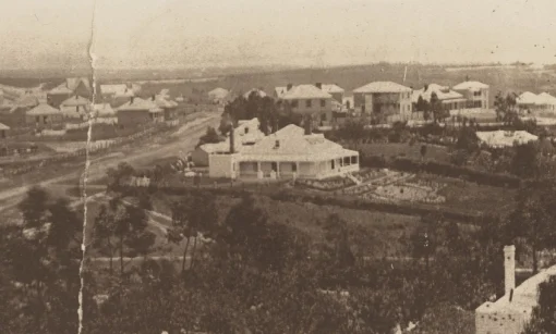 A blurry black and white photo of early Auckland showing wooden dwellings and a dirt road. 