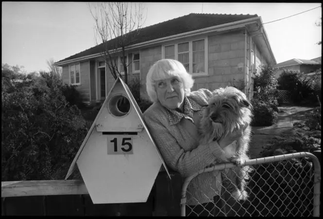 Mrs Zeta Tutt standing at the gate of her State house with her dog Benji, Naenae - Photograph taken by Phil Reid. Dominion post (Newspaper) :Photographic negatives and prints of the Evening Post and Dominion newspapers. Ref: EP/1992/3218/35