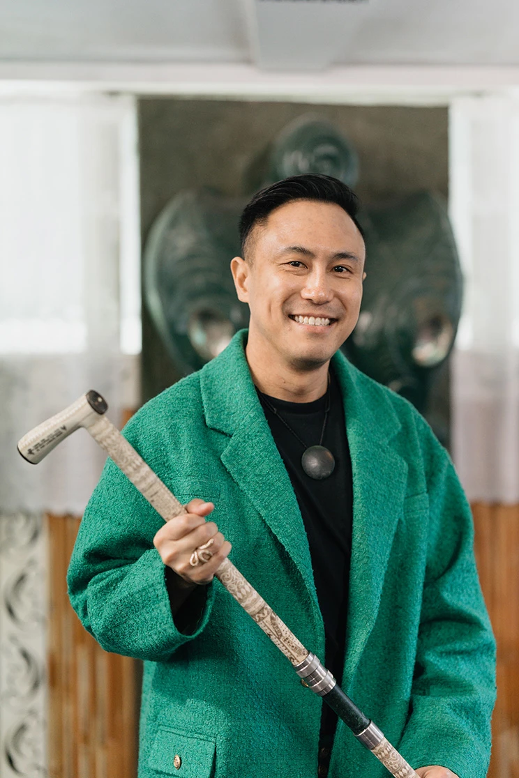 Chris Tse, smiling and wearing a green jacket, holding a carved tokotoko.