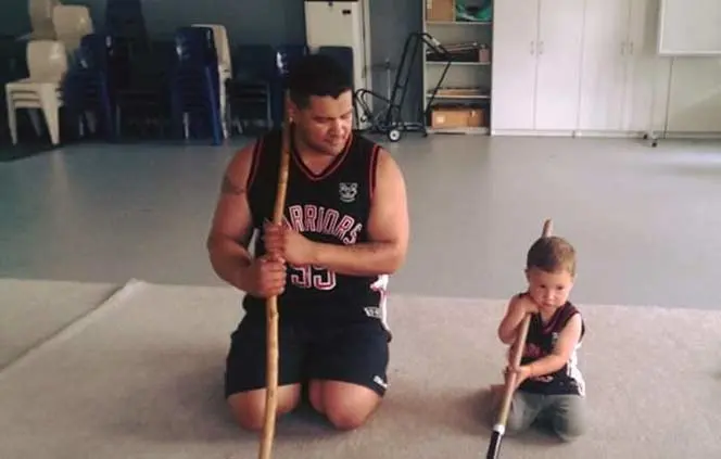 A man and child kneeling holding spearlike weapons.