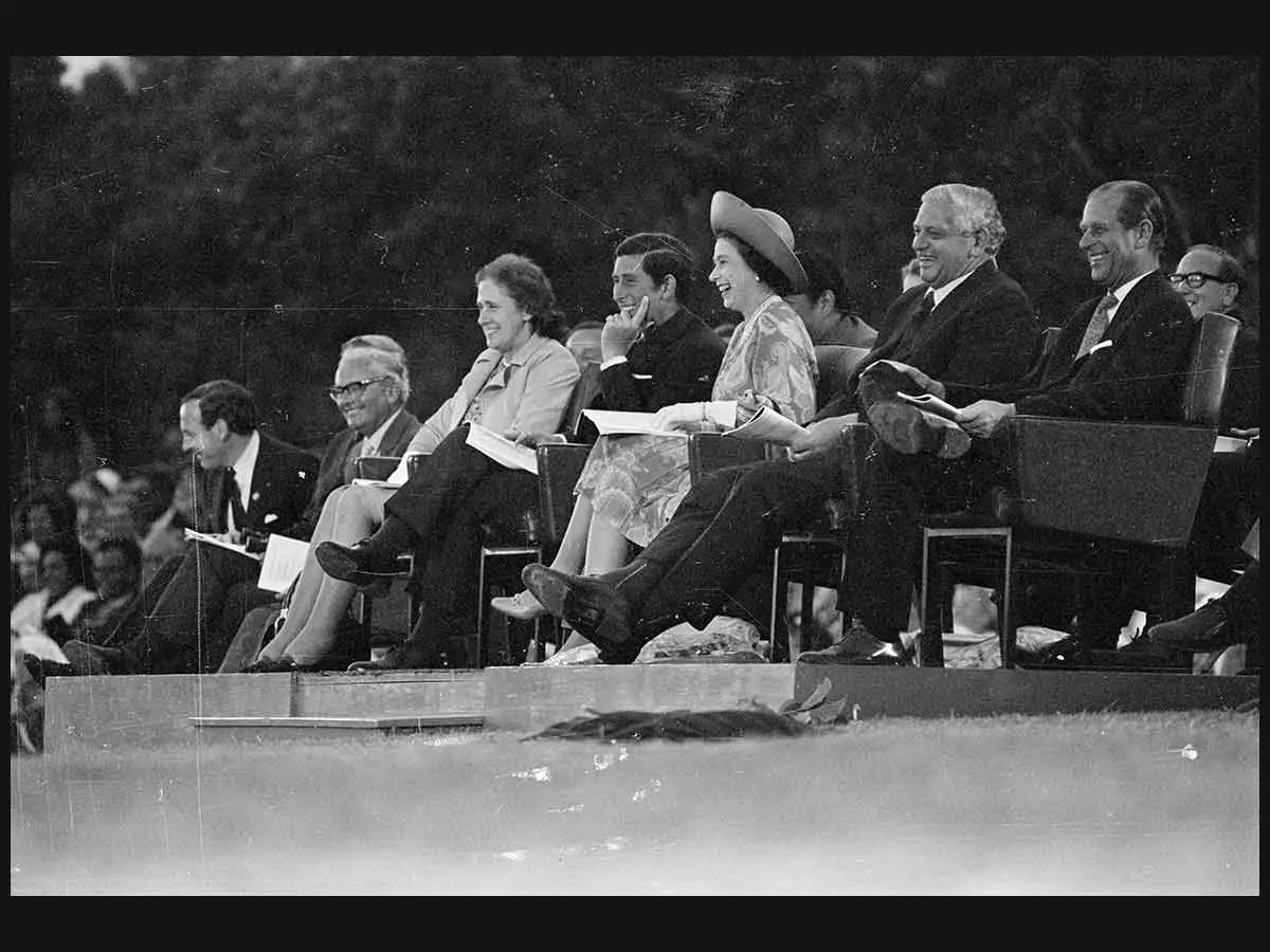 A black and white photo of Prince Charles, Queen Elizabeth II, Prime Minister Norman Kirk and Prince Phillip seated, watching an event.