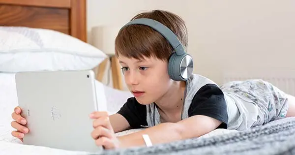 Boy lying on a bed using a tablet and wearing headphones.