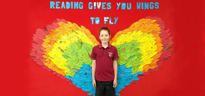 Student in front of a display of wings and with the words 'Reading gives you wings to fly