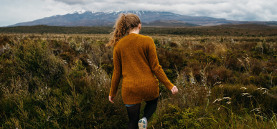 Tongariro peak shrouded in clouds in the background with a girl in brown jersey stepping towards the mountain in the foreground