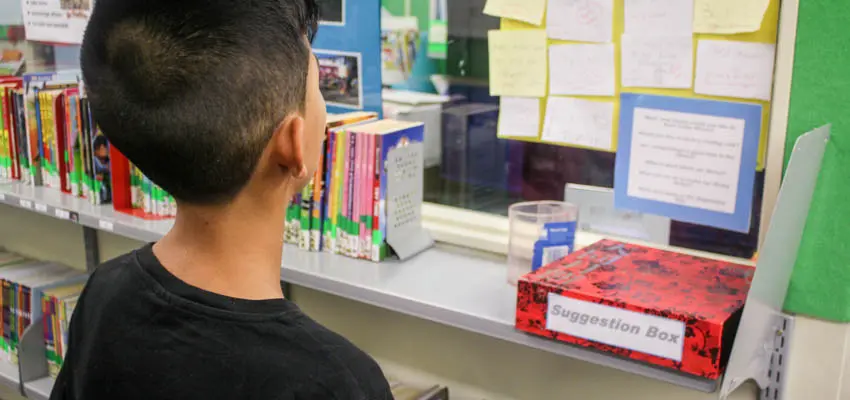 Boy in school library looking at suggestion box.