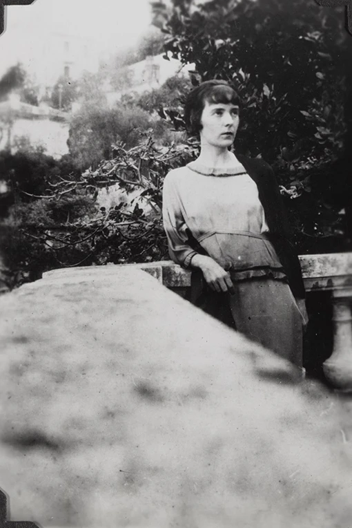 A woman with short dark hair on a verandah with a large tree in the background.