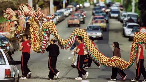A Chinese giant dragon puppet being carried by 5 people across a street.