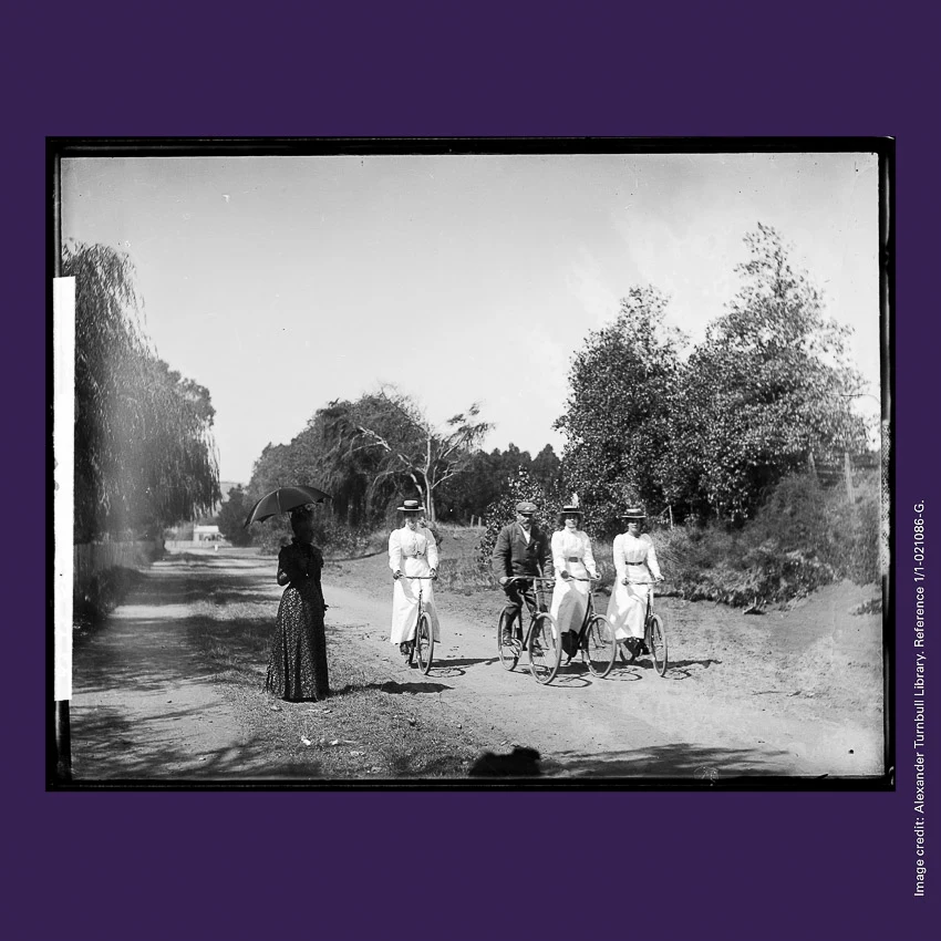 Front of curiosity card CC0009, featuring three women in white and one man riding bicycles abreast down a dirt road while passing a strolling woman with an umbrella