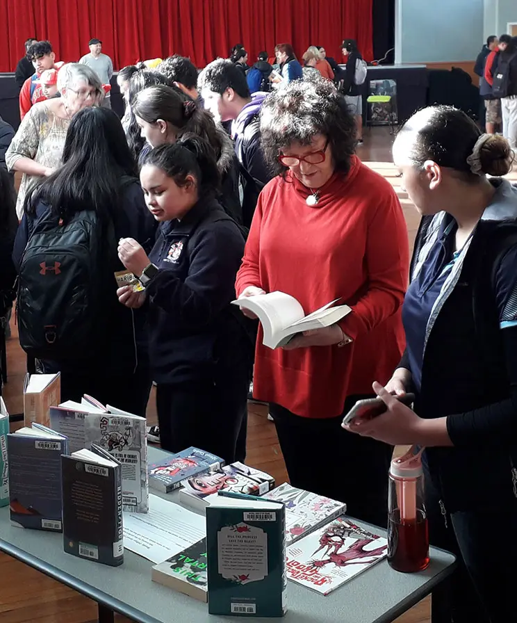 A Pākehā woman and Māori students looking at books on a table.