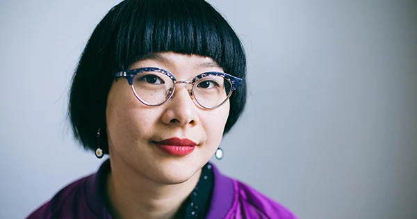 Close up photo of a Chinese woman wearing tortoiseshell glasses and a purple jacket.