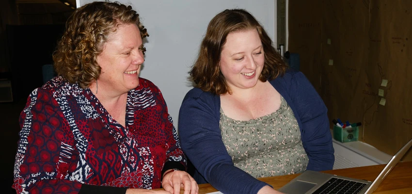 Two people smiling one with a loan form looking at a laptop.