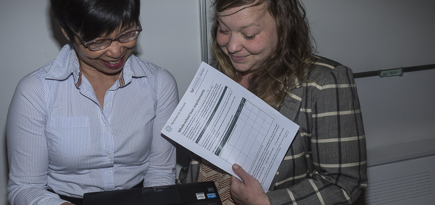 Two people smiling one with a loan form looking at a laptop.