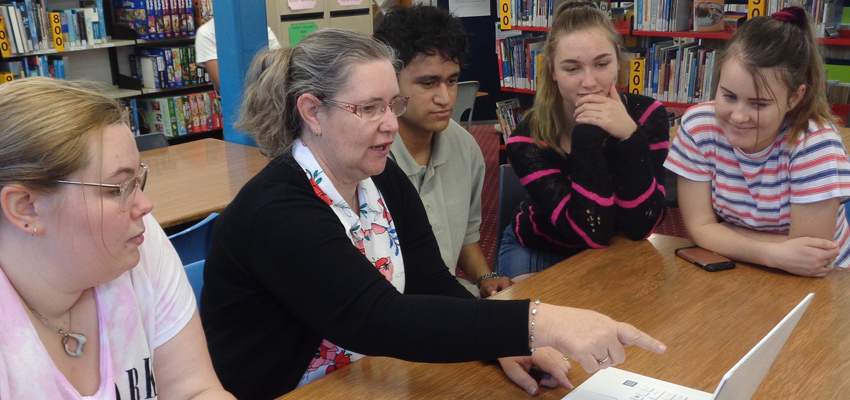 Librarian and 4 students in the school library, looking at a computer screen