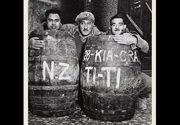 3 soldiers from the 28th (Māori) Battalion peering out from behind 2 barrels of tītī (muttonbirds).