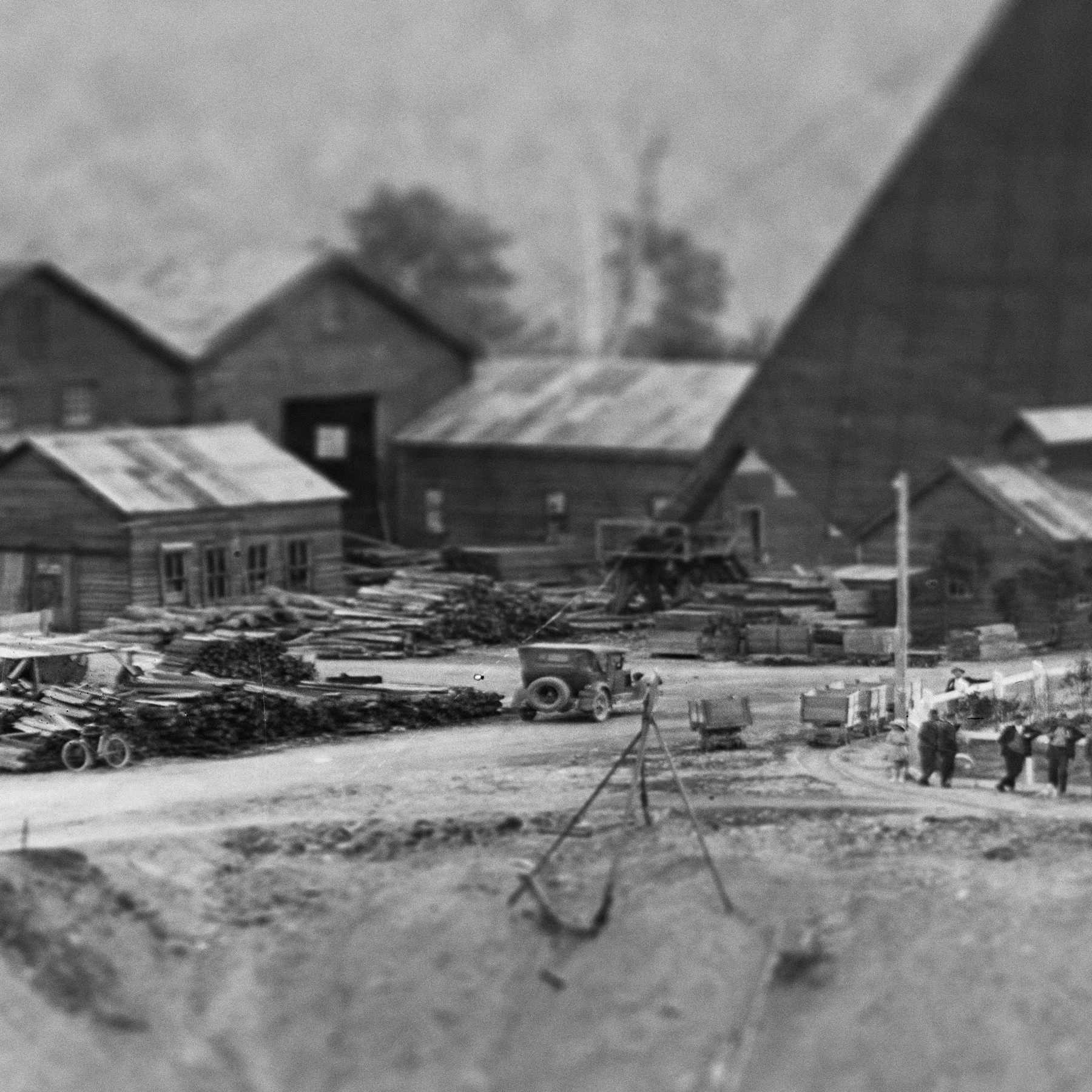 A small group of people can be seen standing on the site of a mine with piles of timber and a car and bicycle all visible.