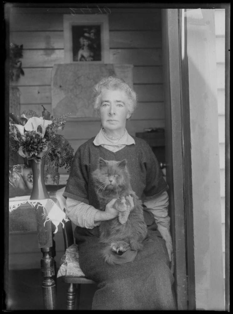 A woman sits on a chair posing for the camera with a cat in her lap.