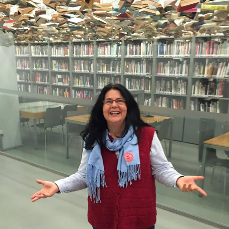 Woman standing in front of books with her arms out and a big smile. There are lots of books hanging like clouds above her head. 