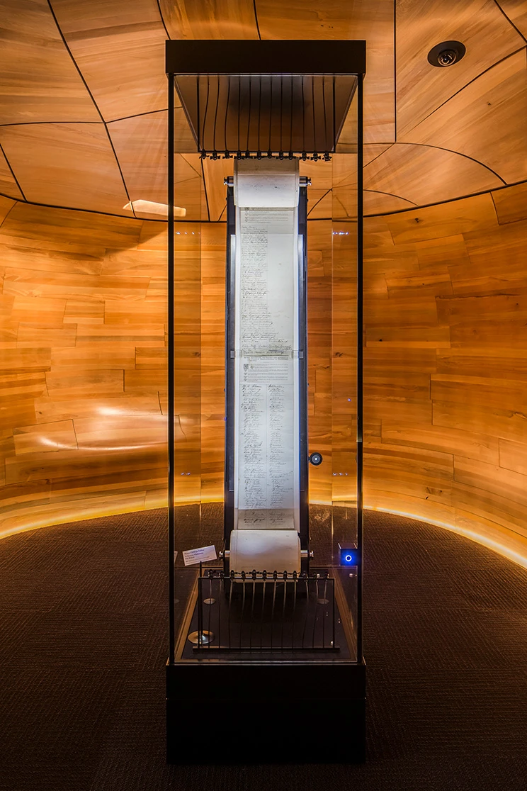 A scroll with a number of signatures displayed in a room with wooden walls and ceiling.