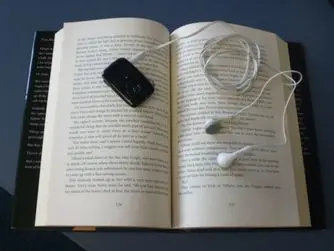 An mp3 player with headphones attached laying on top of an open book.
