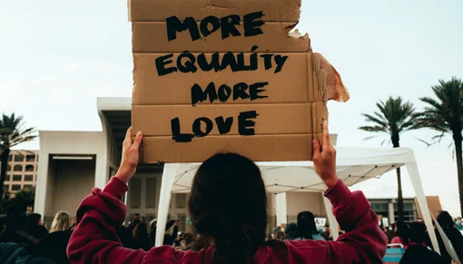 A placard reading 'more equality more love' being held up at a social justice protest.