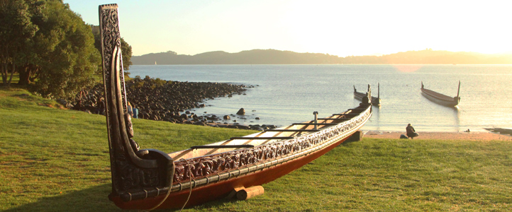 Carved Māori waka on beach with water and waka in background