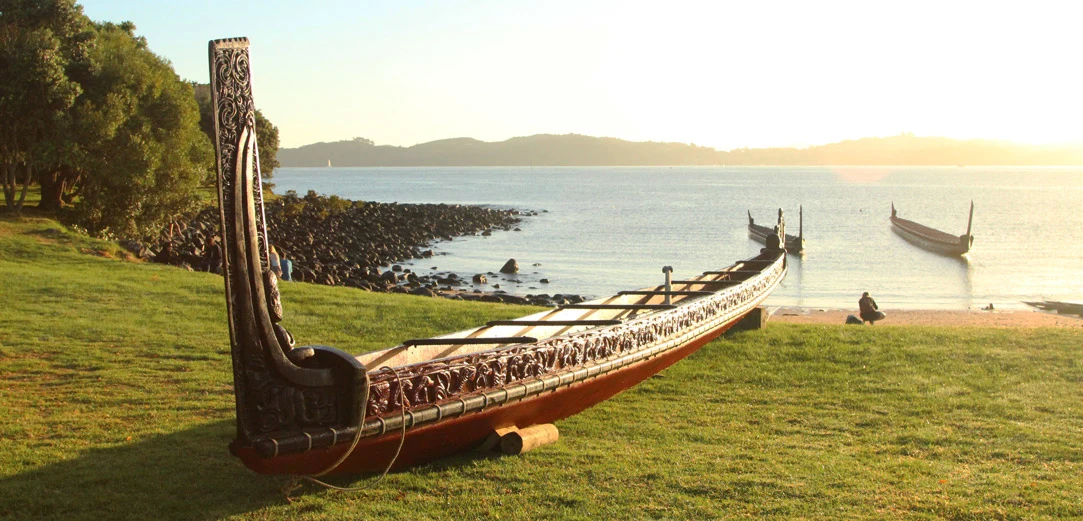 Carved Māori waka on beach with water and waka in background