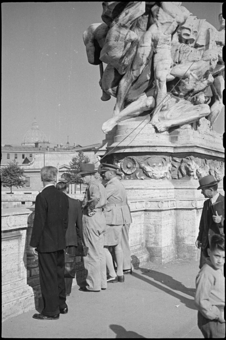 A few men dressed in khaki uniforms stand beside a large, marble statue.